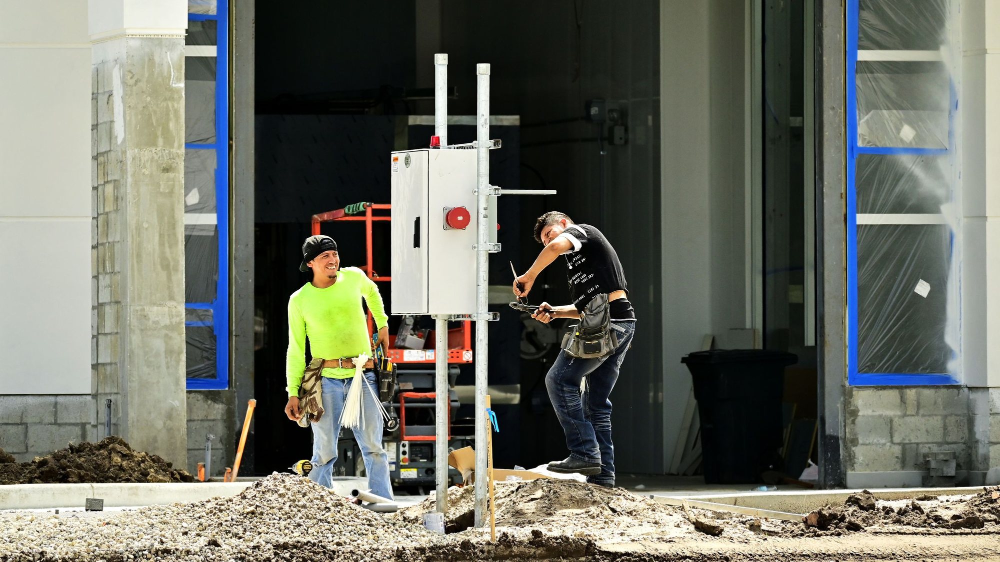Two electricians setting temporary power at a commercial building under construction.